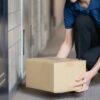 集合住宅の玄関前に置き配の荷物を置こうとしている配達員の手