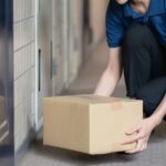 集合住宅の玄関前に置き配の荷物を置こうとしている配達員の手