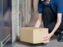 集合住宅の玄関前に置き配の荷物を置こうとしている配達員の手
