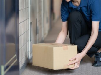 集合住宅の玄関前に置き配の荷物を置こうとしている配達員の手