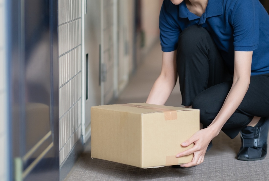 集合住宅の玄関前に置き配の荷物を置こうとしている配達員の手